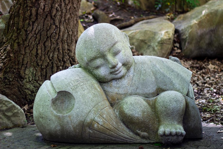 Houten meditatiebeeld naast kabbelend water.